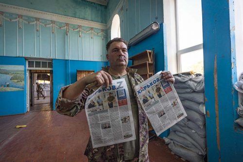 Ukraine, September 2022. Russian newspapers left by the troops inside the house of culture where they had their headquarters. Soldiers from the Ukrainian volunteer army walk in front among the ruins of the city of IzyumThe Ukrainian city of Izium (Izyum) is related  with the mass burial site discovered near by. But there are people still living there. Russia heavily bombarded the town. In  September, its forces left the area leaving behind destroyed infrastructure and a population with no food and no water and under shock.