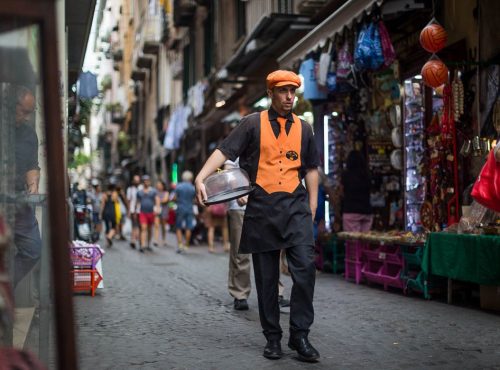 Naples, Italy, a man who deleaver coffees is wolking down the street,.